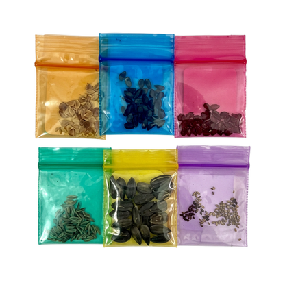 Six small translucent resealable pouches arranged in a 2x3 grid on a white background, each in a different color: amber, blue, pink, teal, yellow, and lavender. The pouches contain small dark seeds or seed-like pieces.